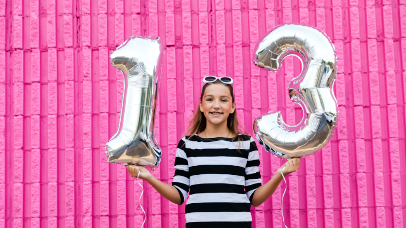 girl holding balloons to say "13" against a pink wall